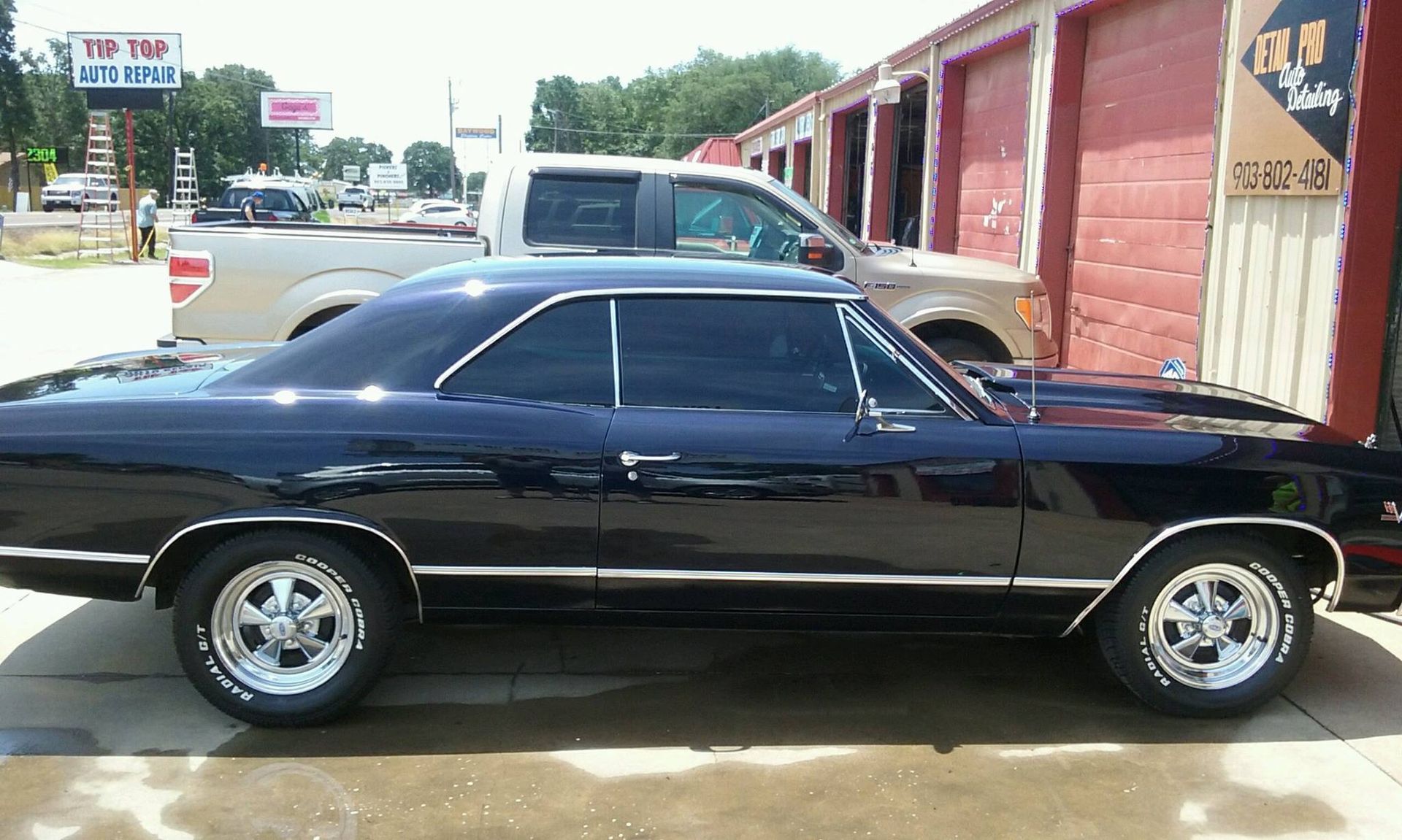 A black car is parked on the side of the road next to a truck.