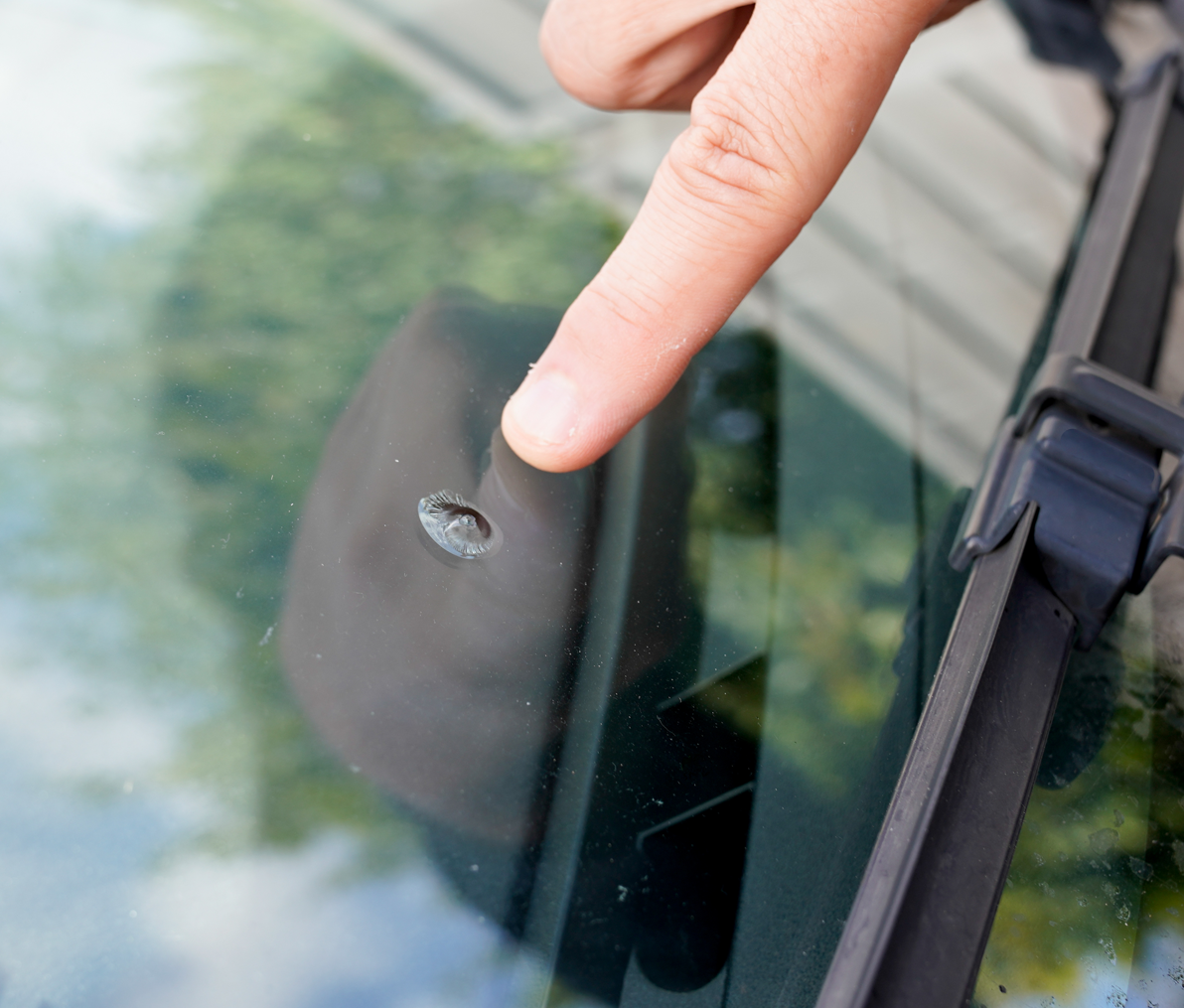 A person pointing at a hole in a car windshield