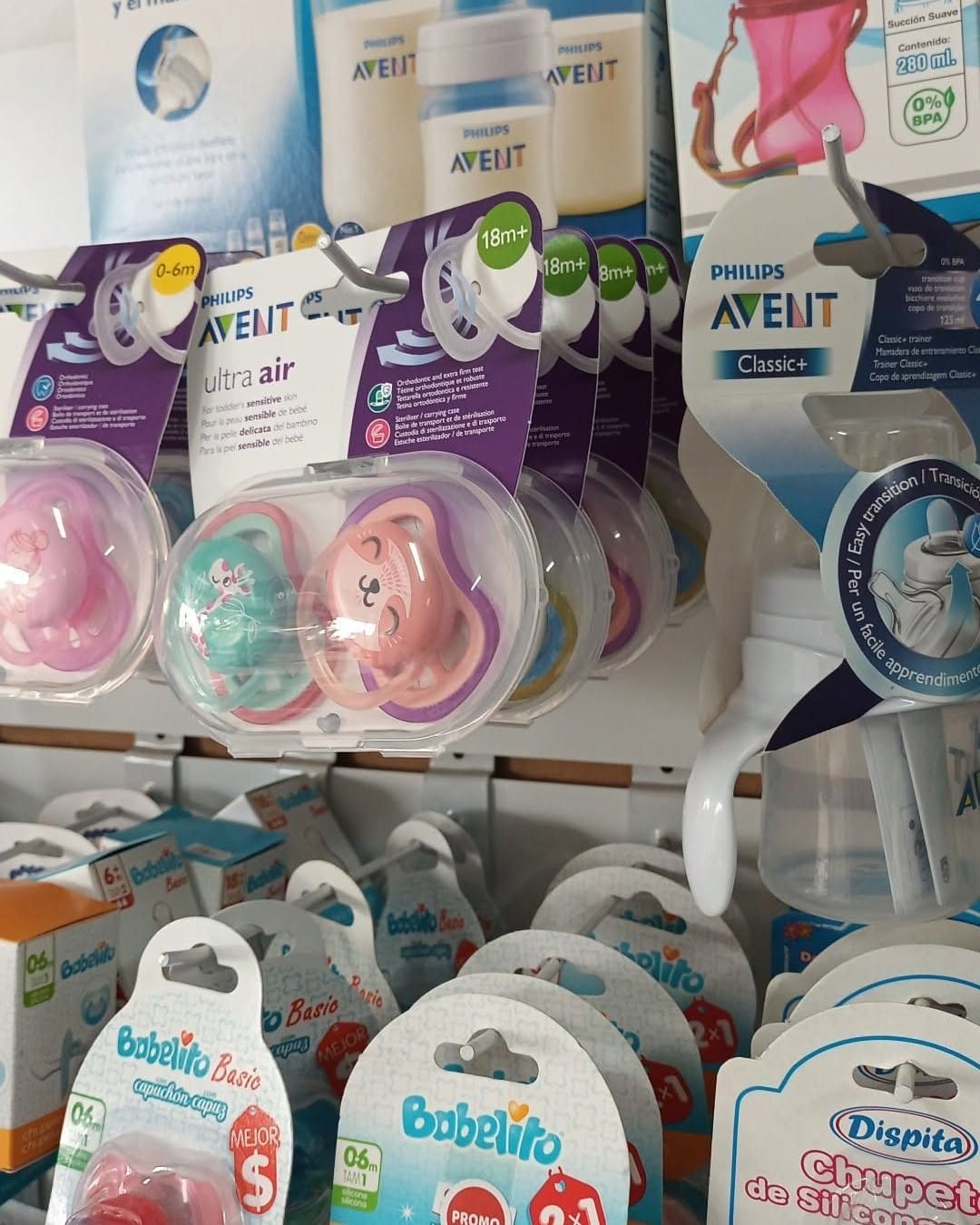 Chupetes en blísteres en un estante de tienda, con envases rosas, azules y morados.
