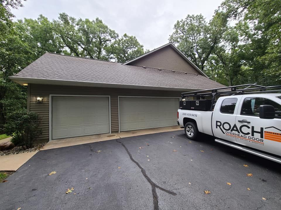 A white roach truck is parked in front of a garage.