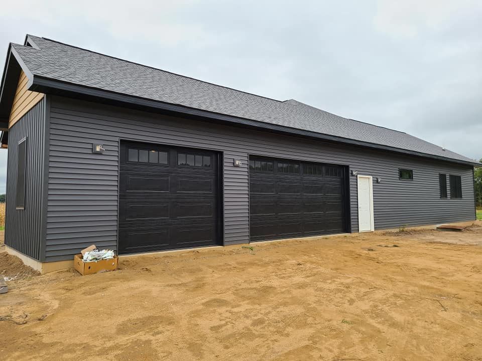 A large garage with three black garage doors is sitting on top of a dirt field.