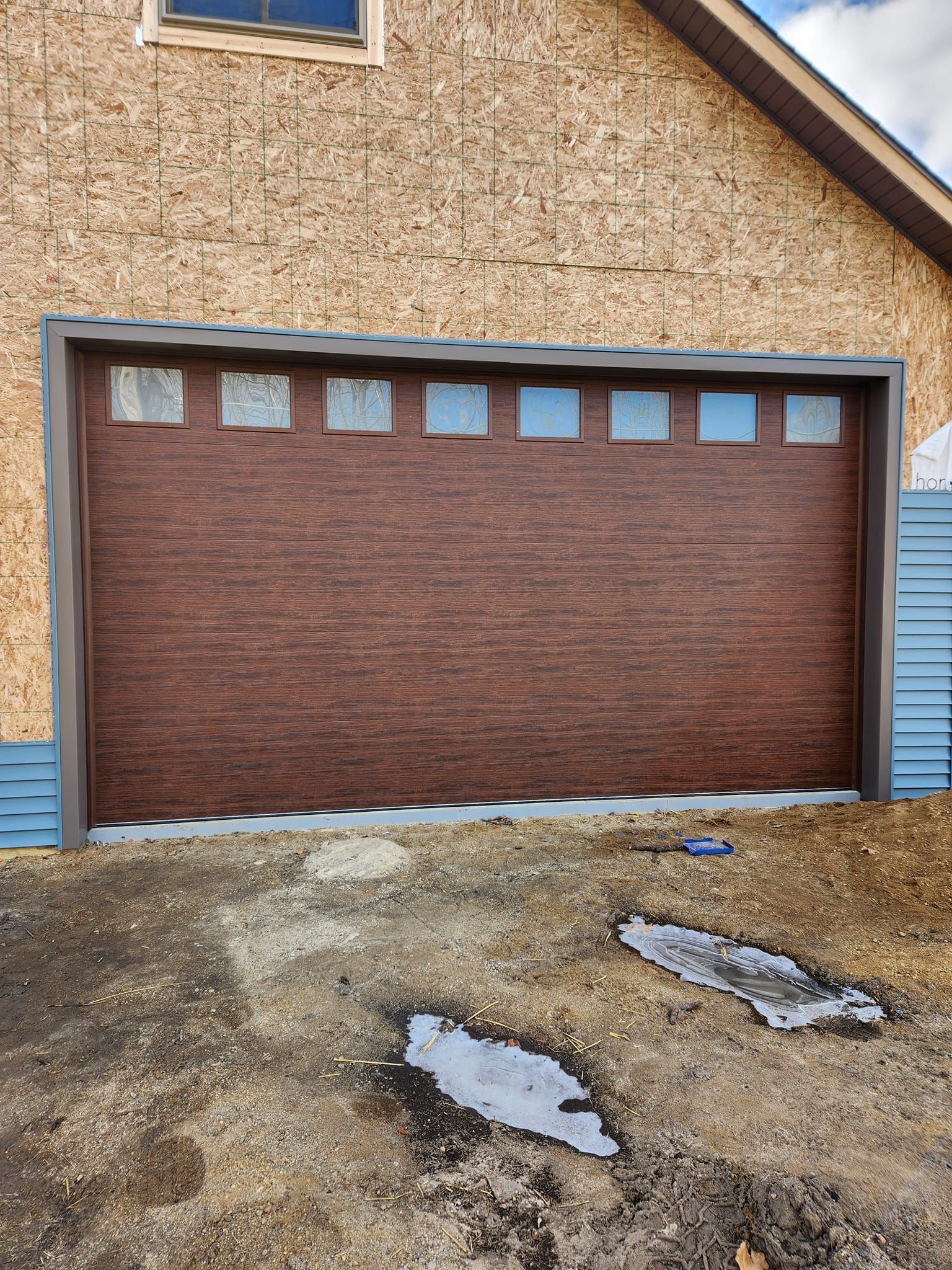 A brown garage door is sitting in front of a house under construction.