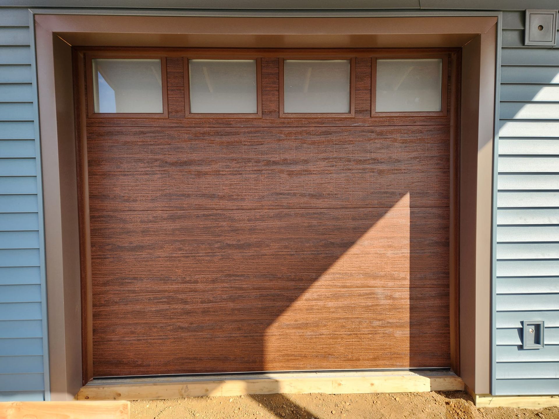 A brown garage door is sitting in front of a blue house.