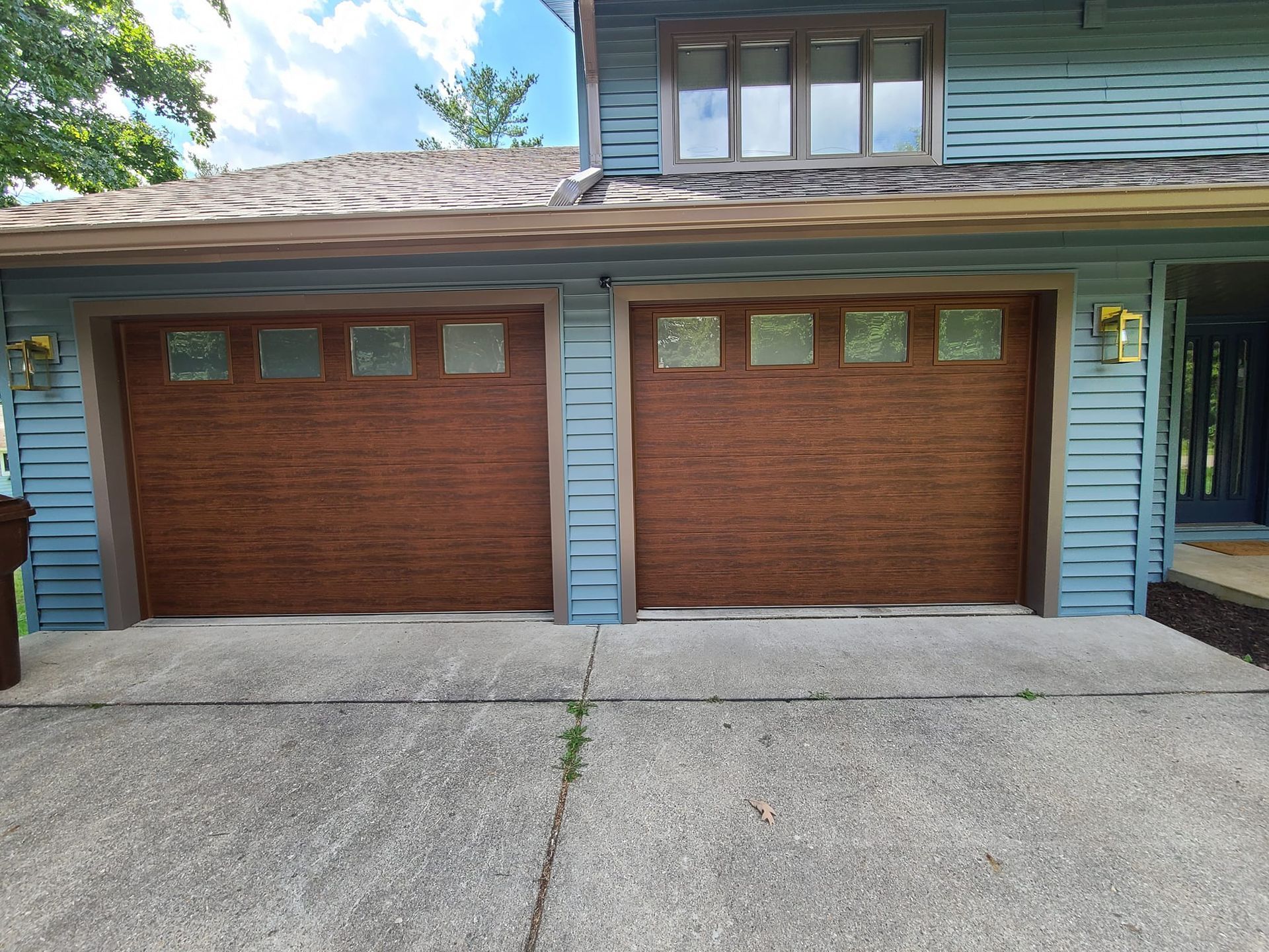 A blue house with two brown garage doors and a concrete driveway.