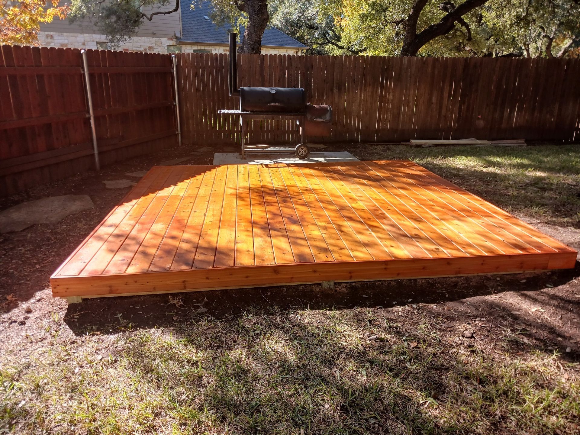 Wooden deck in a backyard with a grill. Brown wooden fence and green grass surround the deck.