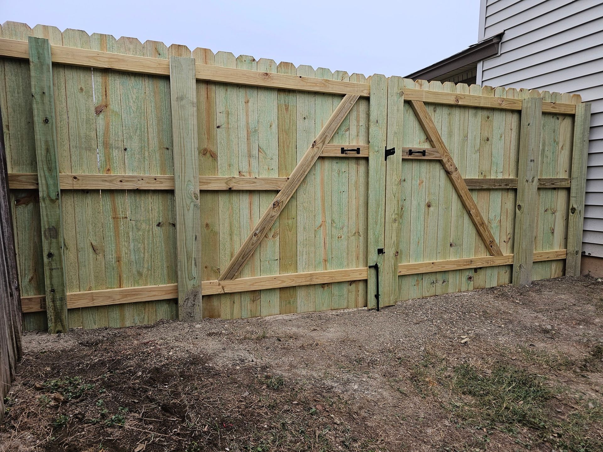 Wooden fence with a gate, built with vertical planks and a decorative scalloped top.