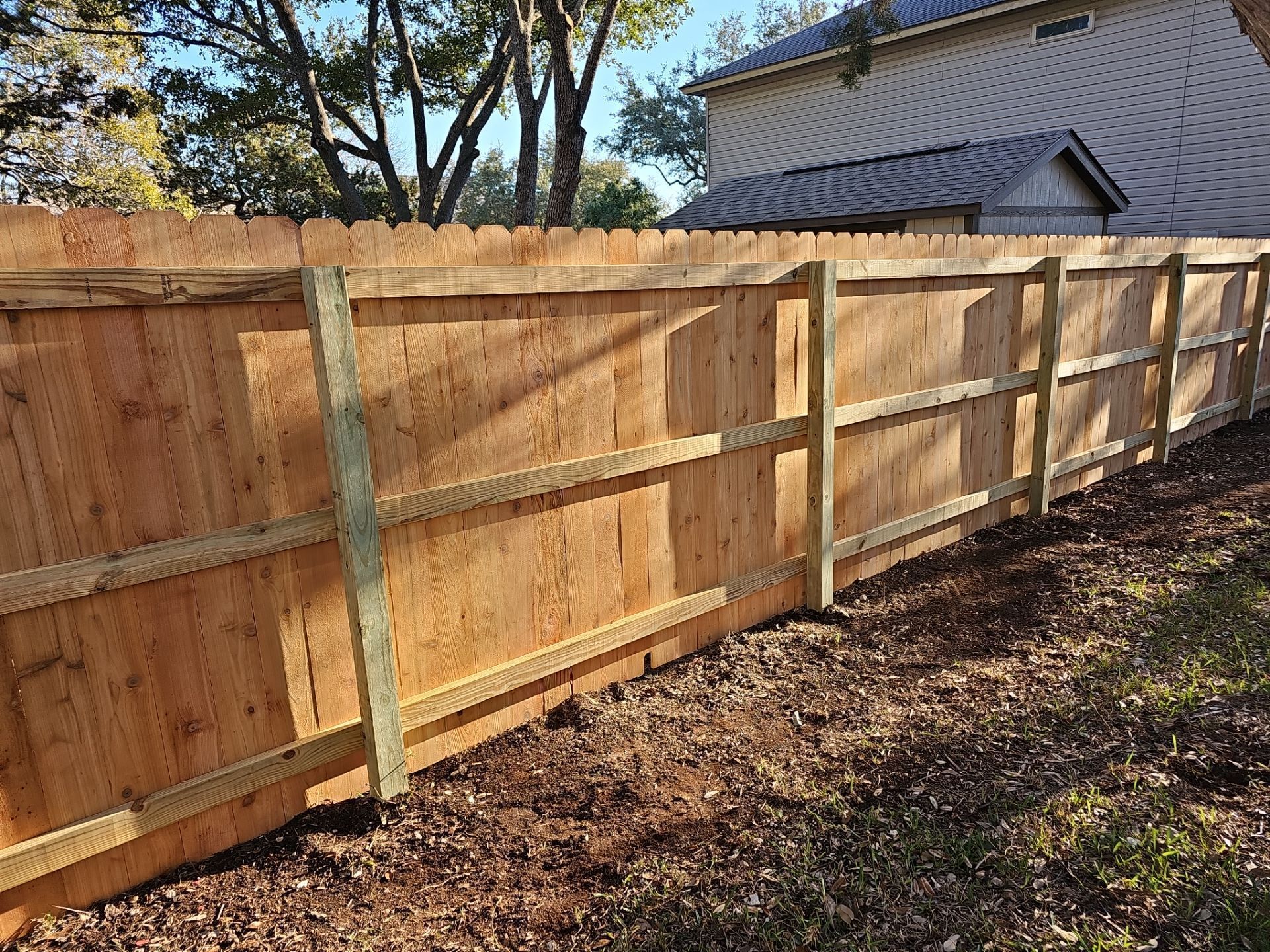 Newly constructed wooden fence in a backyard, with light brown planks and green support posts.