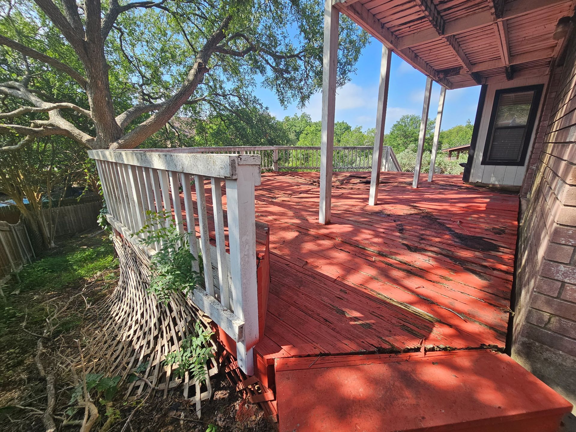 A weathered wooden deck painted red, with white railing, surrounded by trees.