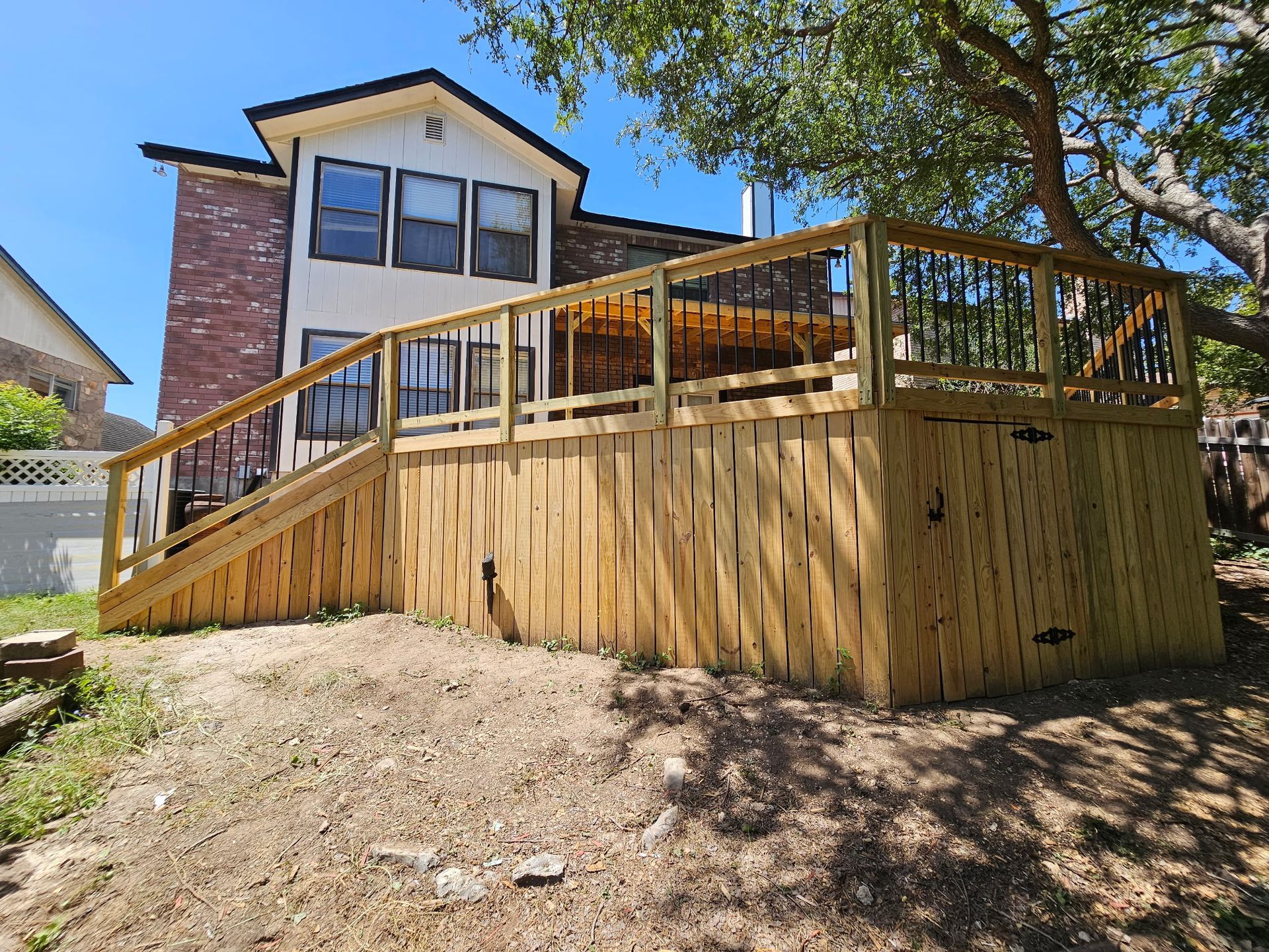 Wooden deck with ramp and railing built against a brick house, on a sunny day.