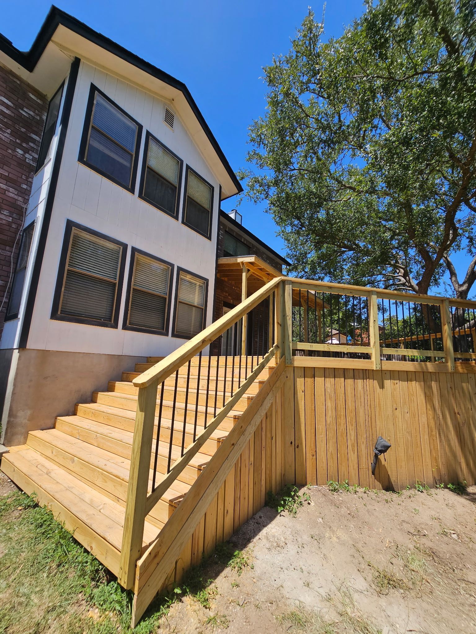 Wooden deck and stairs attached to a white house with black window shutters, under a blue sky.