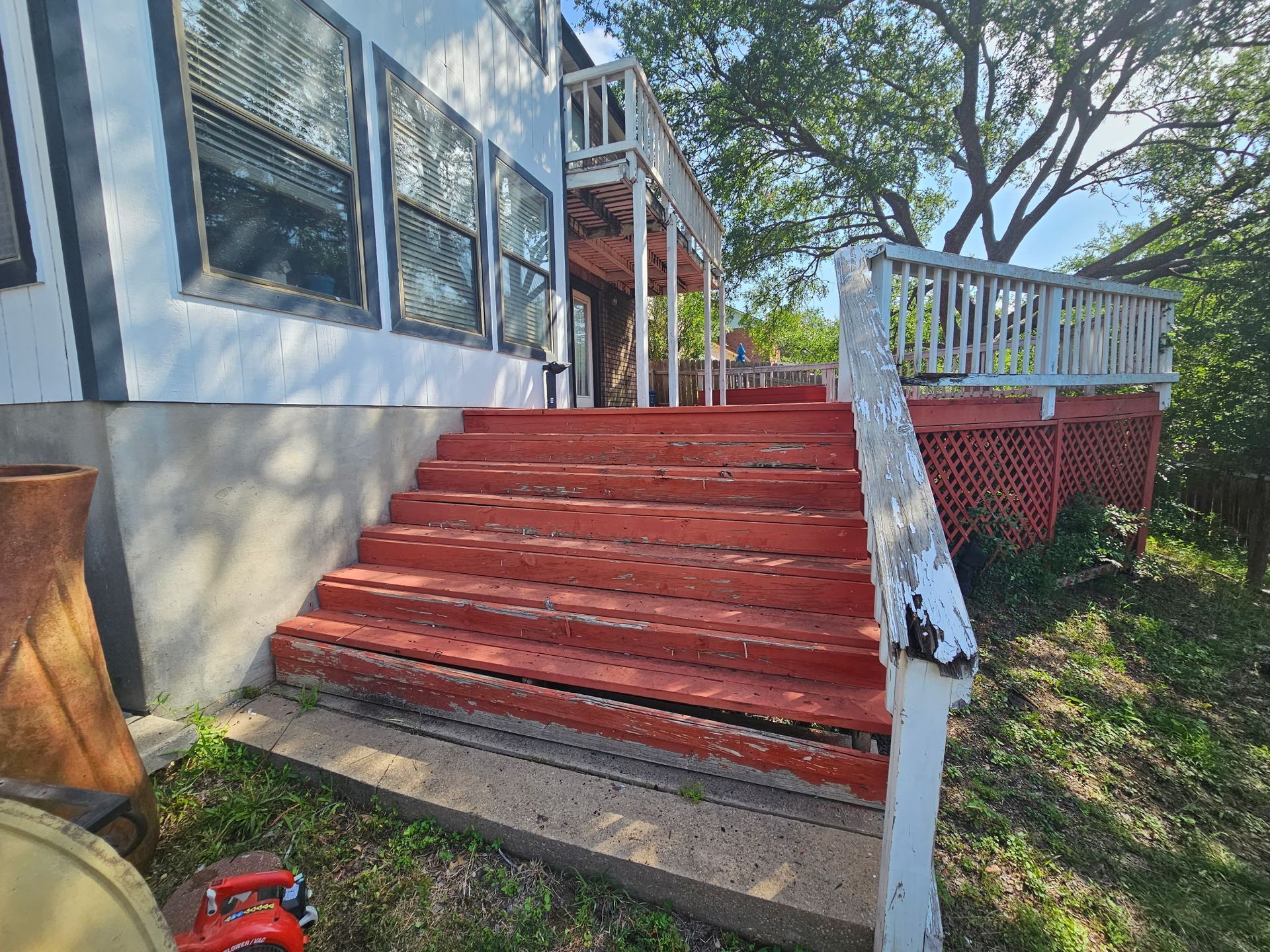 Exterior view of weathered red steps leading to a deck with peeling white railings.
