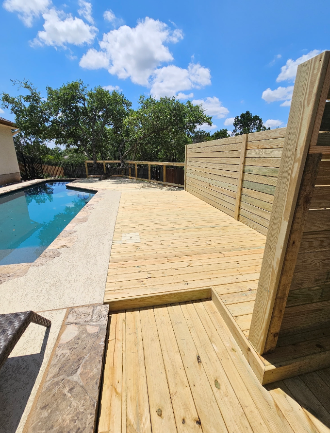 A wooden deck next to a swimming pool on a sunny day