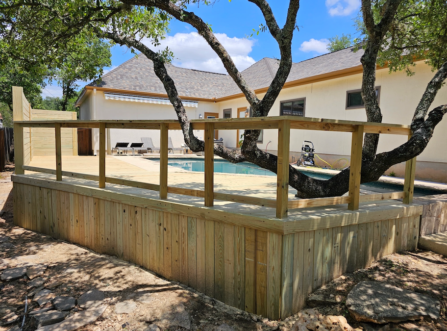 A wooden deck with a fence around it and a pool in the background.