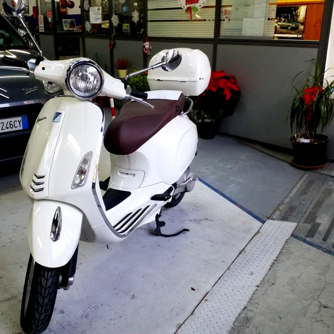 Scooter bianco parcheggiato davanti a un negozio, con sella marrone e casco bianco sul manubrio.