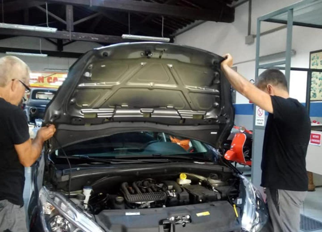 Due meccanici ispezionano un'auto con il cofano aperto in un garage.