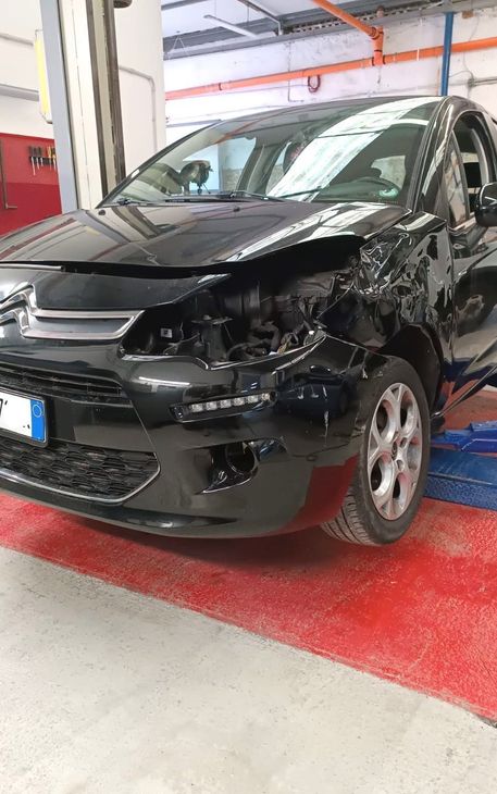 Auto nera con danni alla parte anteriore parcheggiata in un'officina.