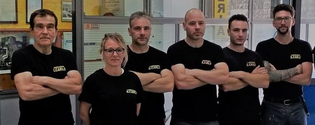 Cinque persone con indosso magliette nere, in piedi con le braccia incrociate, in una palestra o in uno studio.
