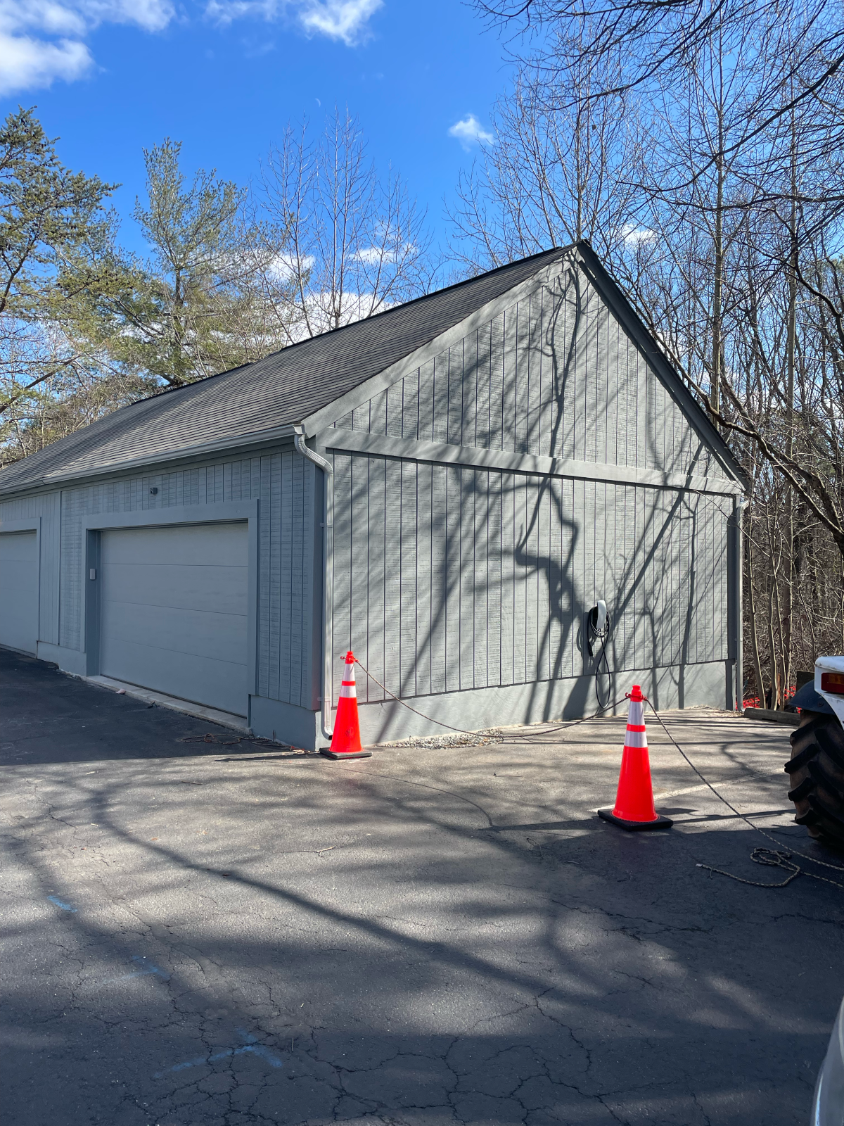 Gray garage with closed door, two orange cones on asphalt driveway, blue sky.