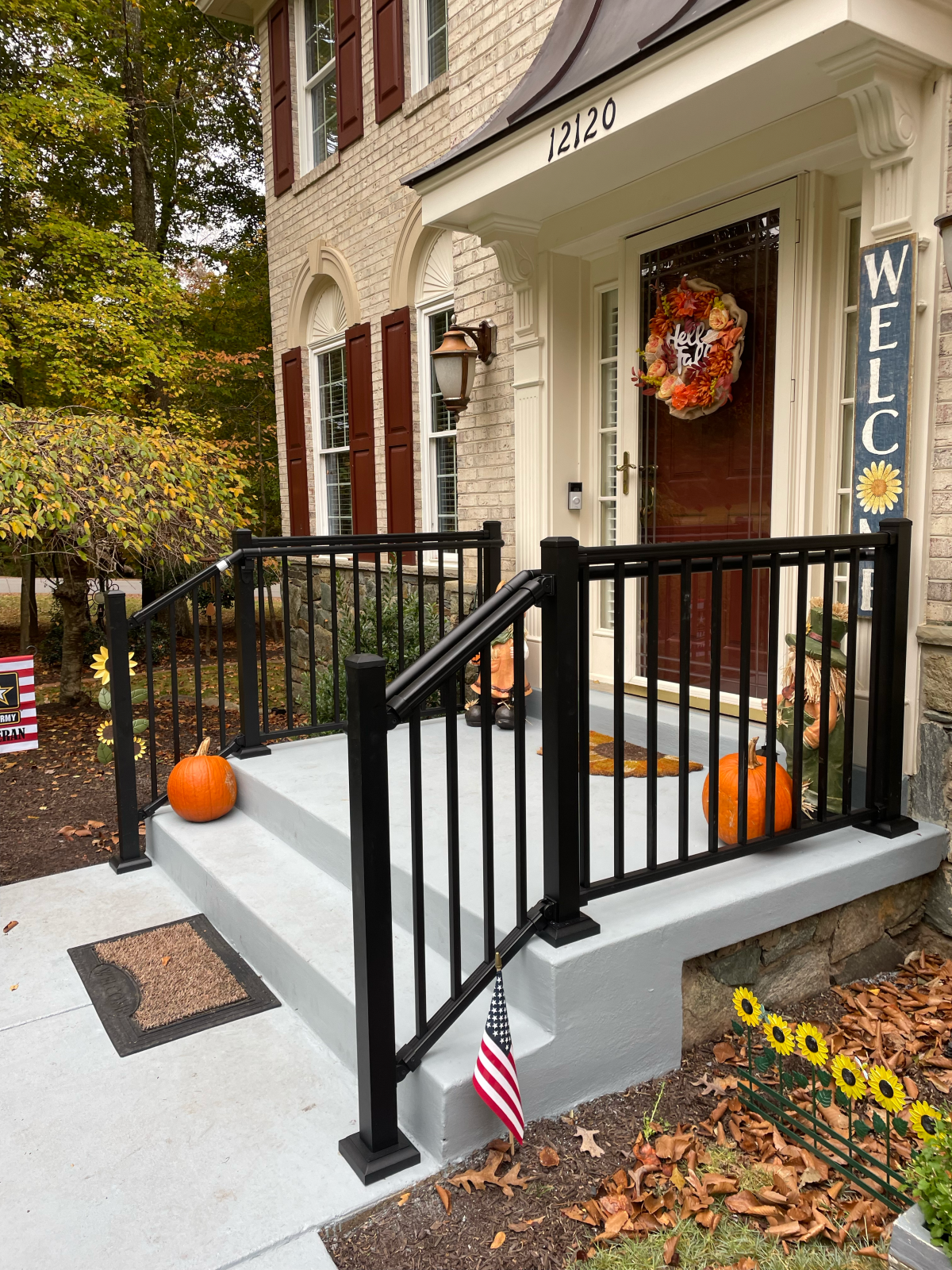 A front porch with black railing, steps, pumpkins, and a fall wreath on the door. 