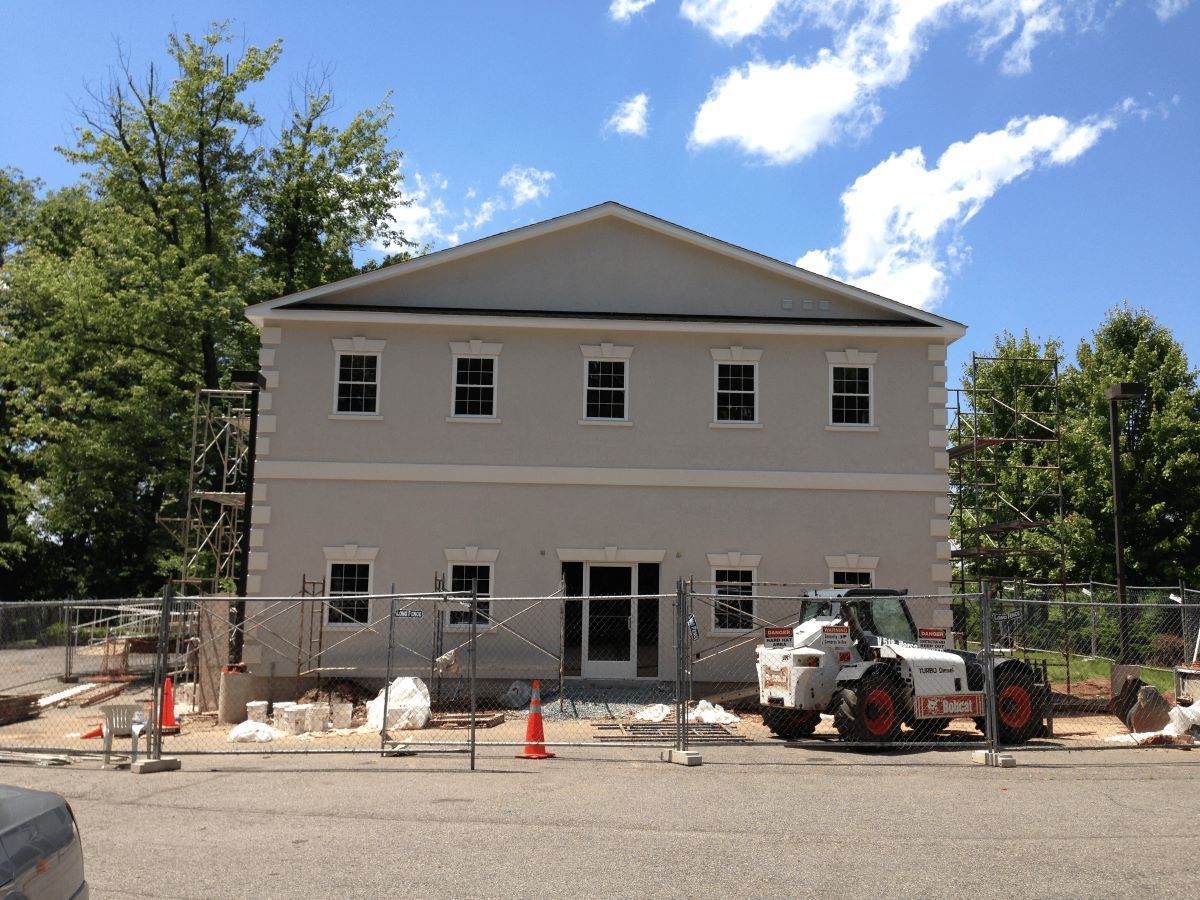 Two-story building under construction with scaffolding and a tractor in front; chain link fence.