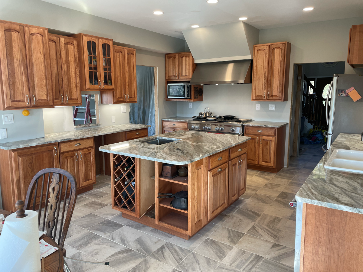 Kitchen with wood cabinets, island, and countertops; appliances; floor tiles; and partially constructed elements.