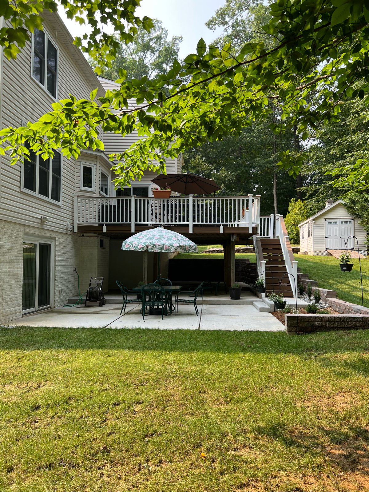 Backyard deck and patio with furniture, lawn, trees, and shed.