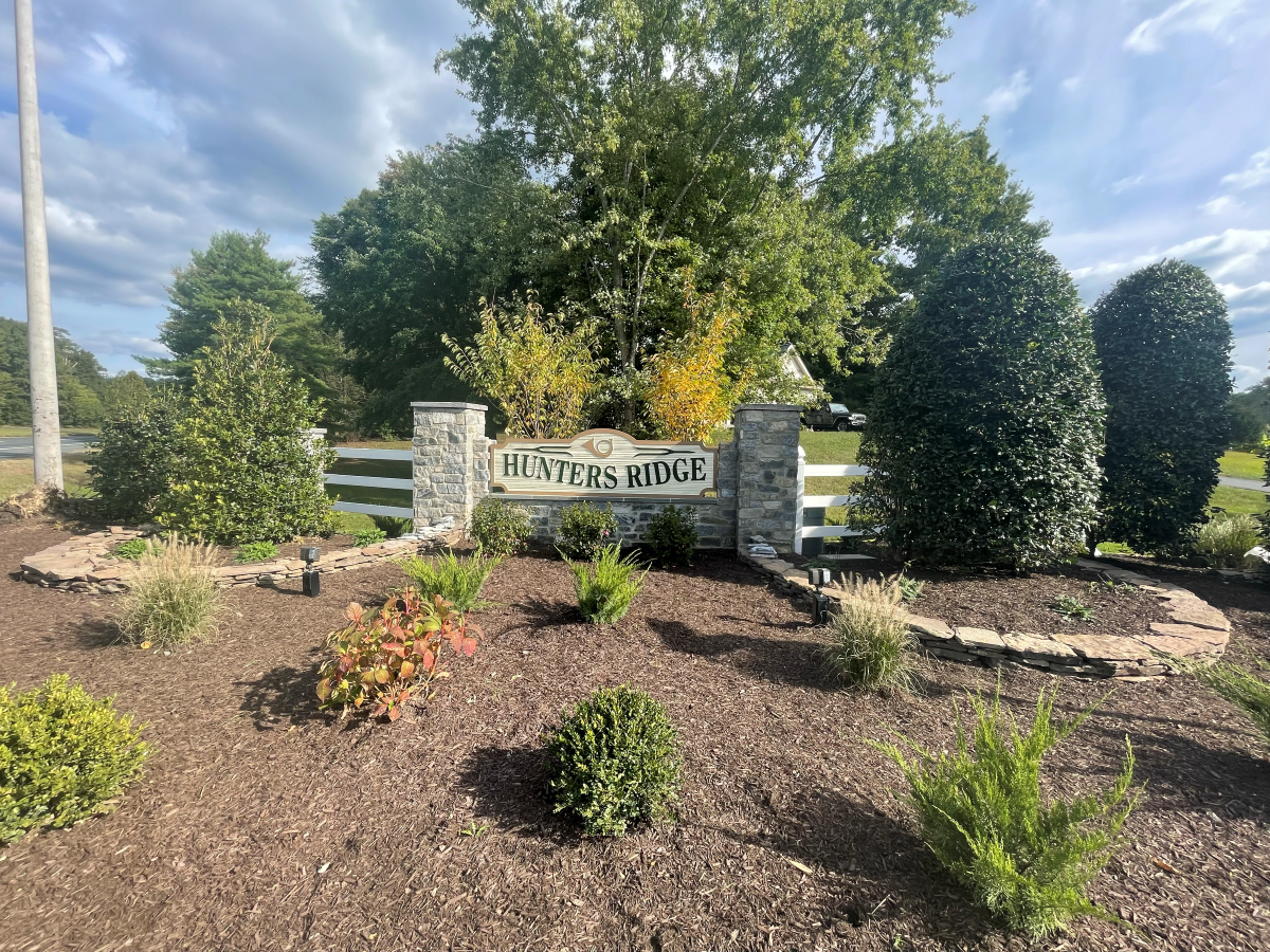 Sign for Hunters Mill, with stone pillars, surrounded by landscaping and fence.
