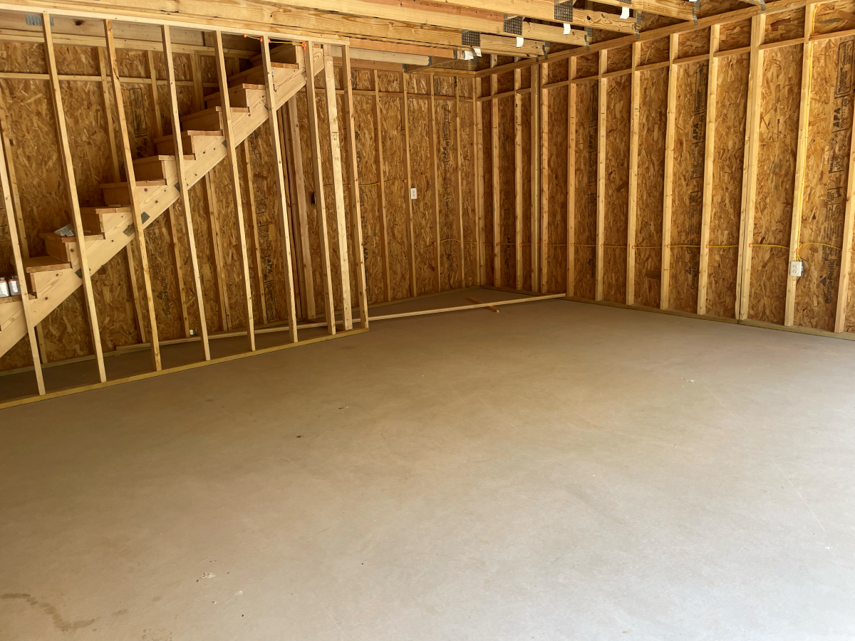 Unfinished room with concrete floor, wood framing, and stairs leading up.
