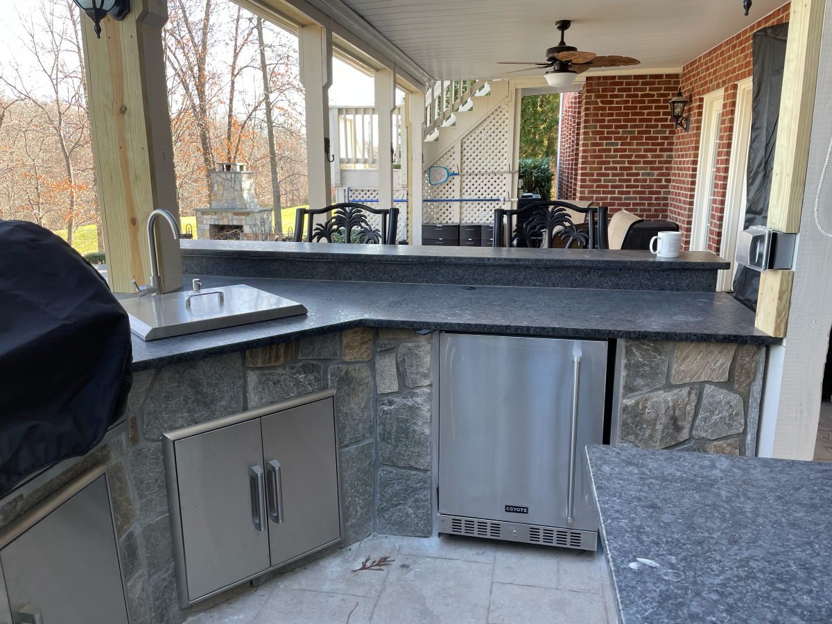 Outdoor kitchen with gray countertop, stainless steel appliances, stone facade.