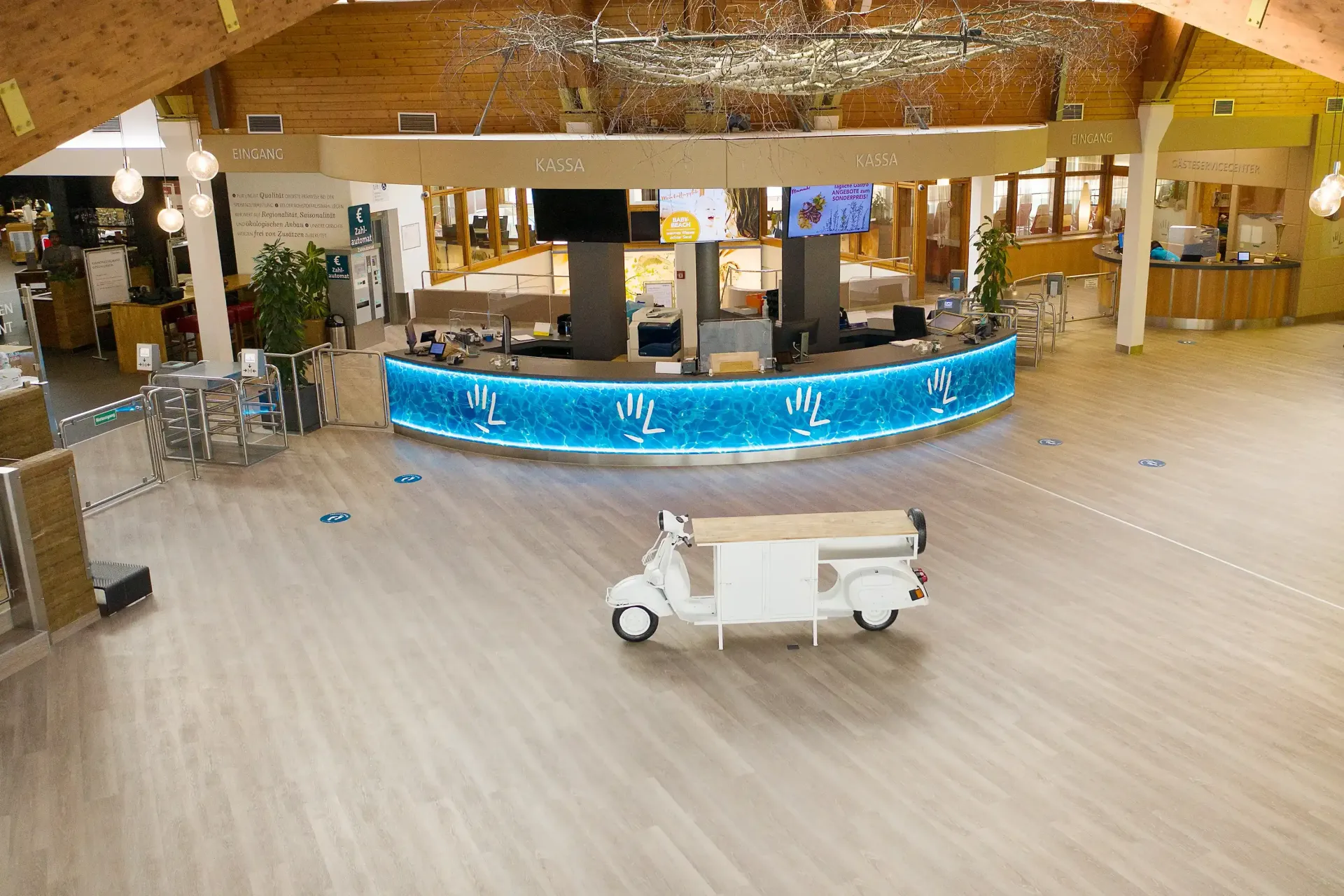 Weißes Fahrzeug auf Holzboden in einem hell erleuchteten, großen Raum mit einer geschwungenen, blau beleuchteten Bar.