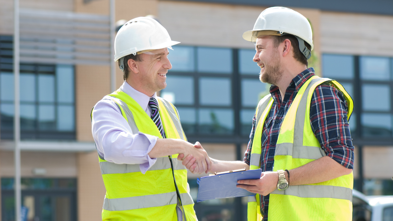 Two electrical contractors are shaking hands on a construction site.