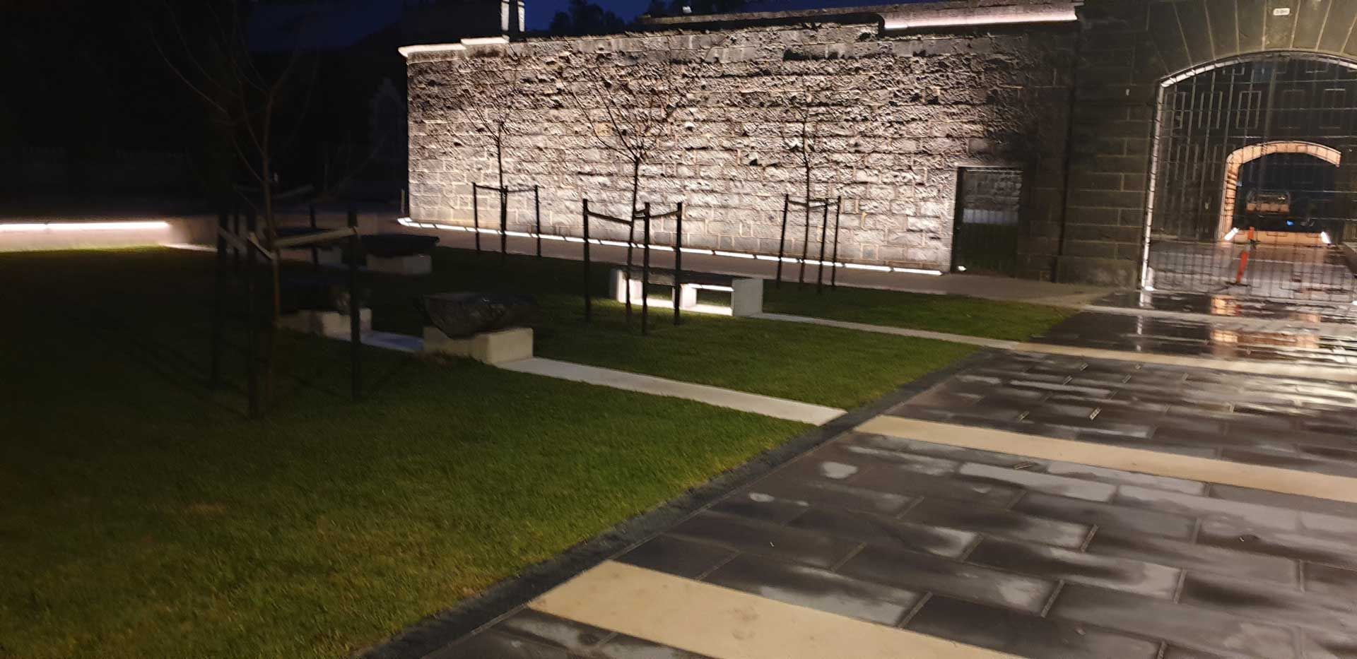 A Brick Wall Is Lit Up At Night In A Backyard