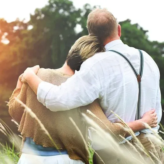 A man and woman are hugging in a field of tall grass.