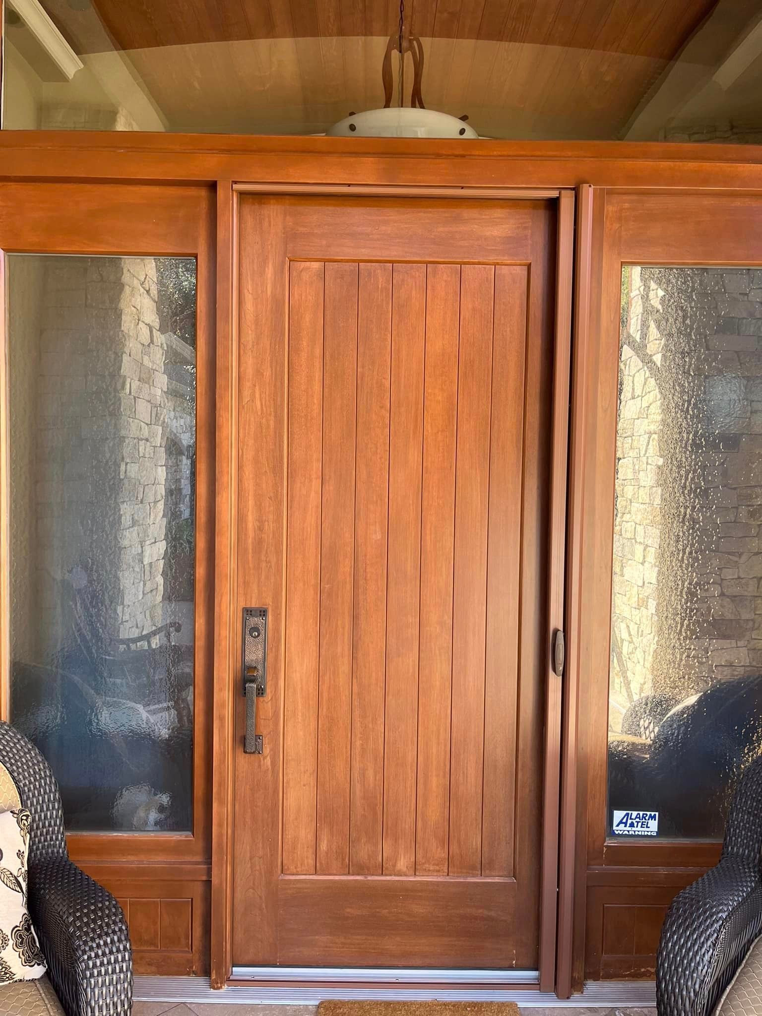 Wooden front door with frosted glass sidelights and a covered porch ceiling above