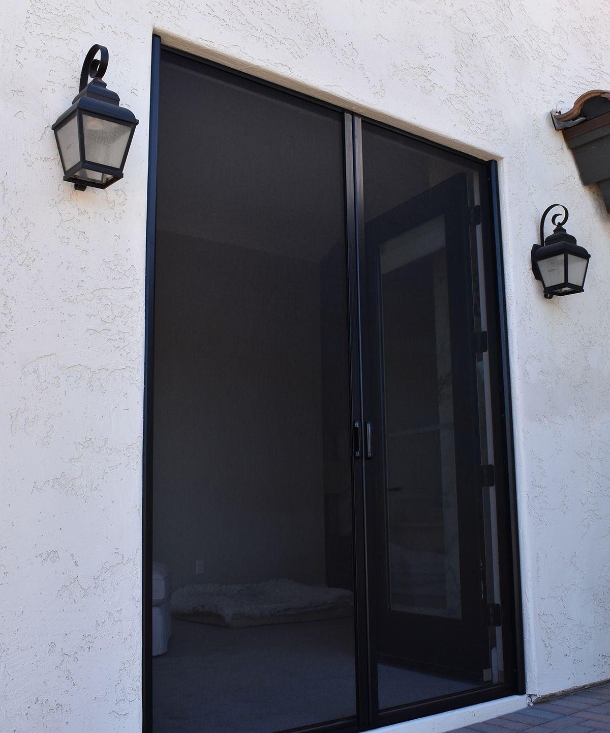 Black sliding glass door framed by white stucco wall with two outdoor lanterns.