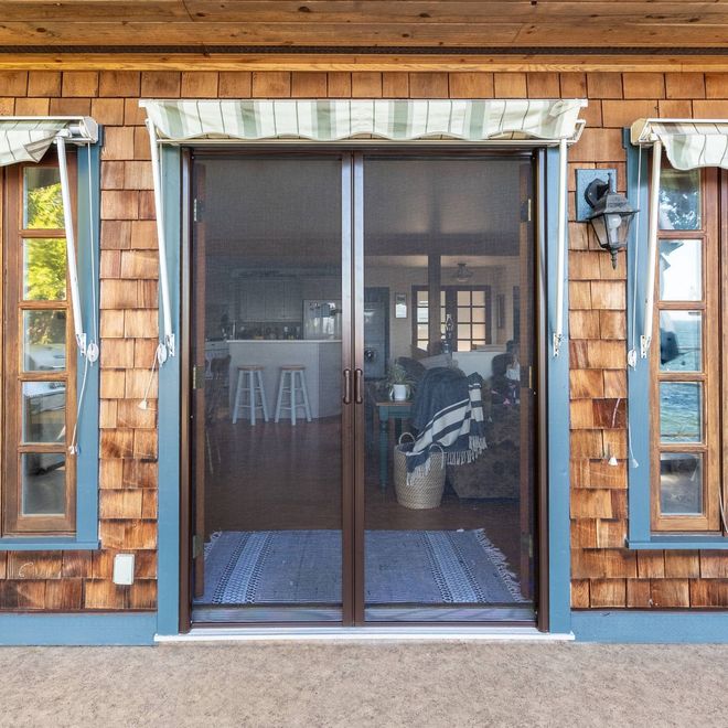 Front view of a screened porch door on a shingled house, flanked by narrow windows.