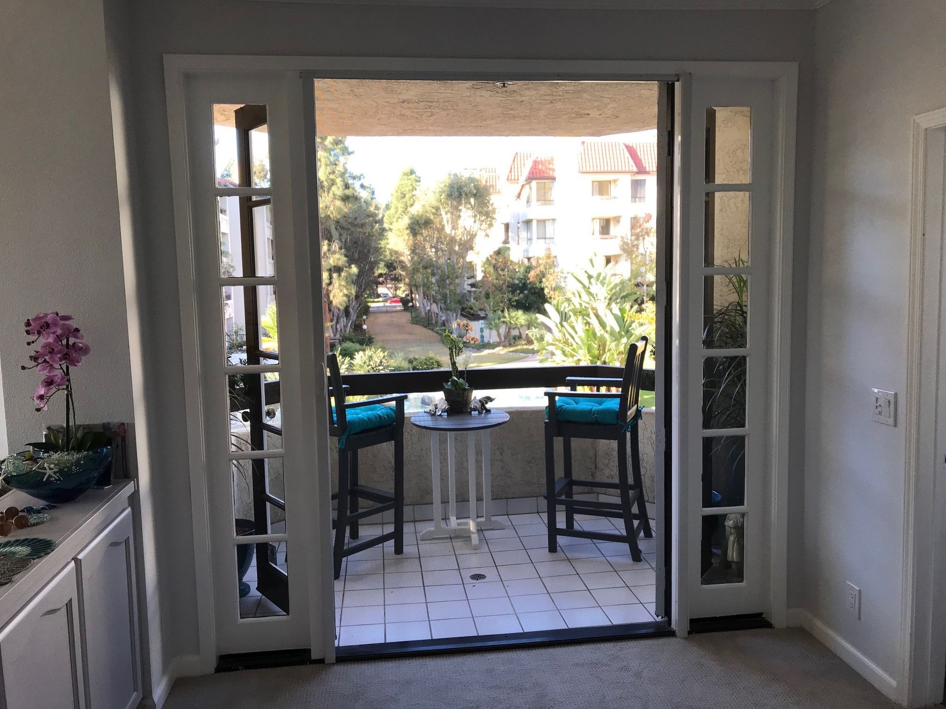 Open French doors to a sunny patio with a table, two stools, and garden view