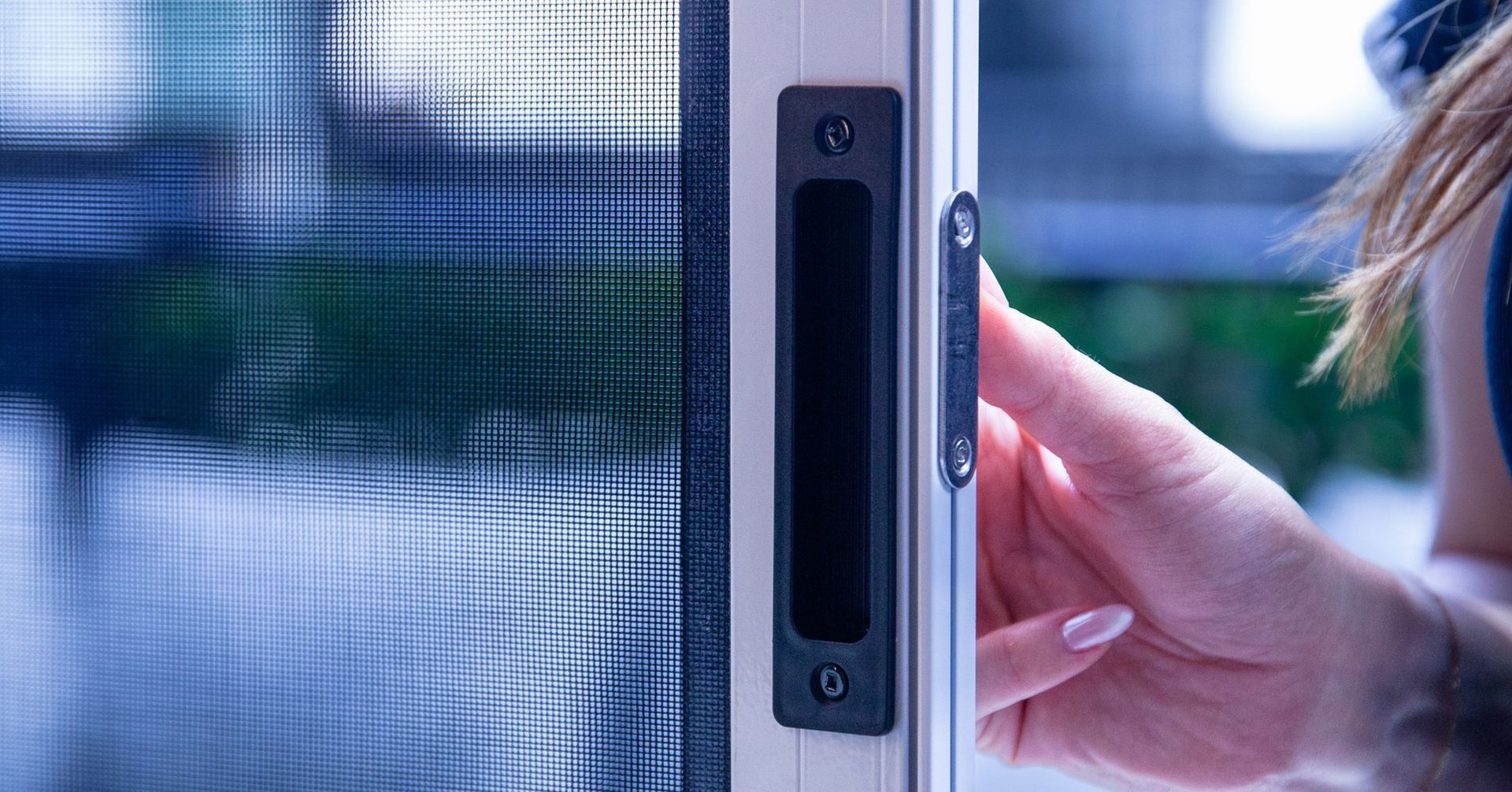 Hand reaching to open a sliding glass door with a black handle and lock mechanism