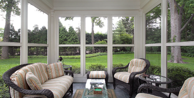 Screened-in porch with wicker seating and glass coffee table overlooking a green backyard
