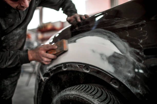 Auto body worker sanding a car fender in a repair shop.
