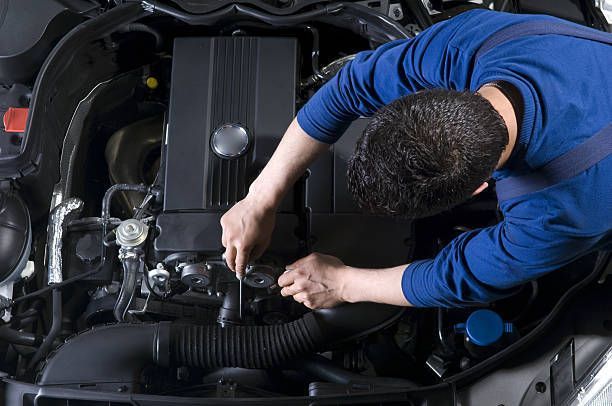 Mechanic in blue uniform working on a car engine in a garage.