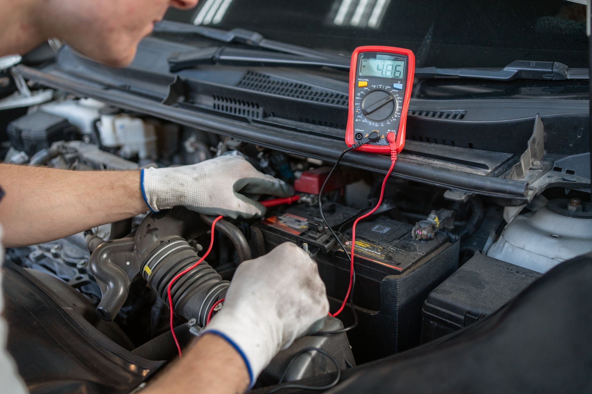 Person using a multimeter to test a car battery in an engine bay.