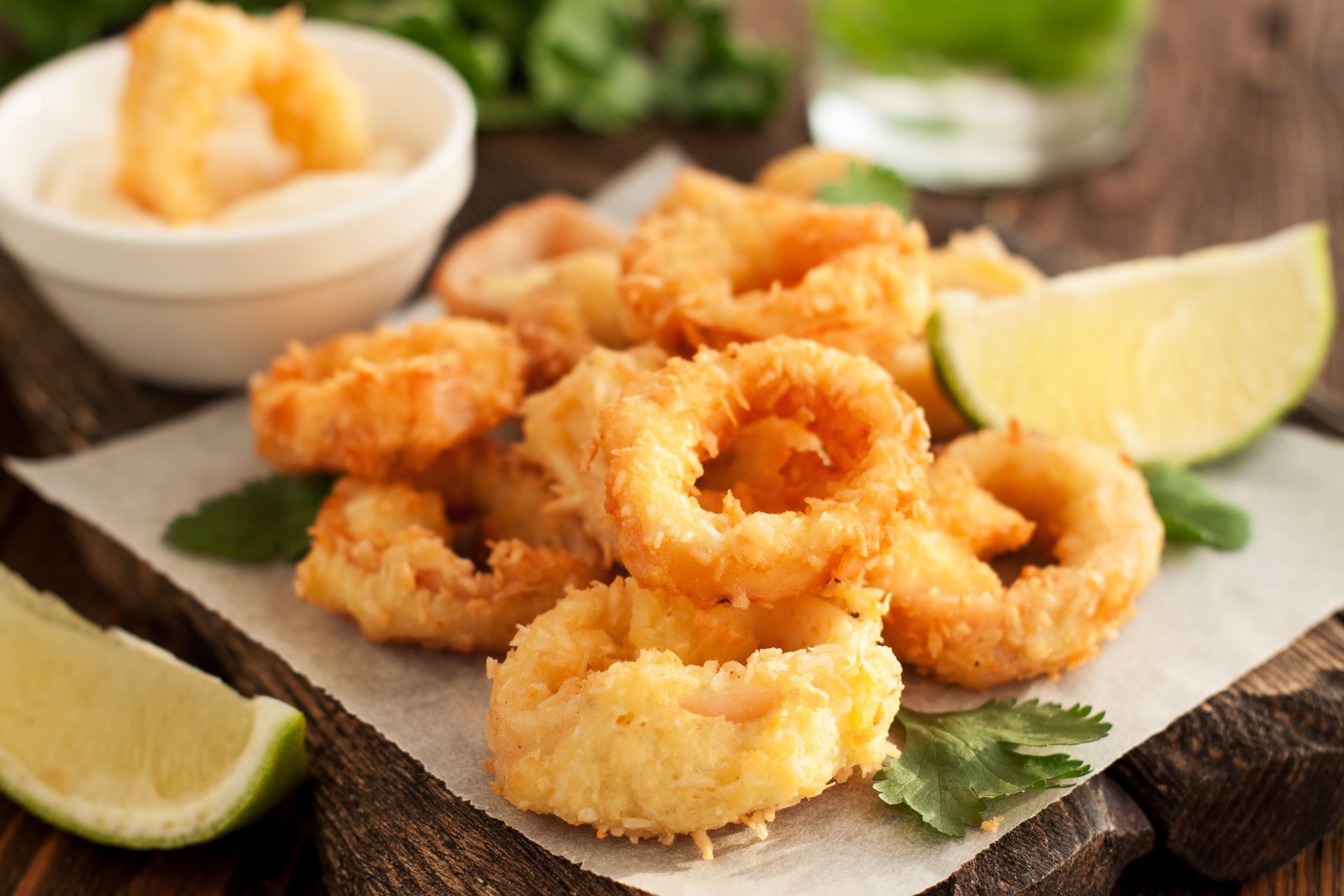 Fried calamari rings with lime wedges and sauce on a wooden table.