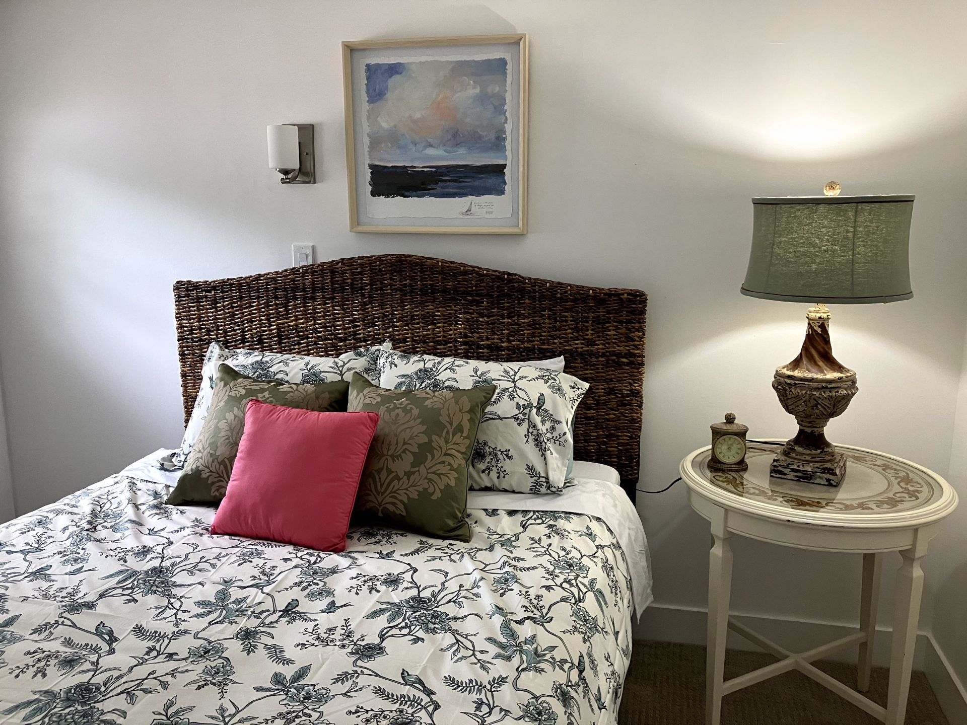 A bedroom with a bed , nightstand , lamp and picture on the wall.