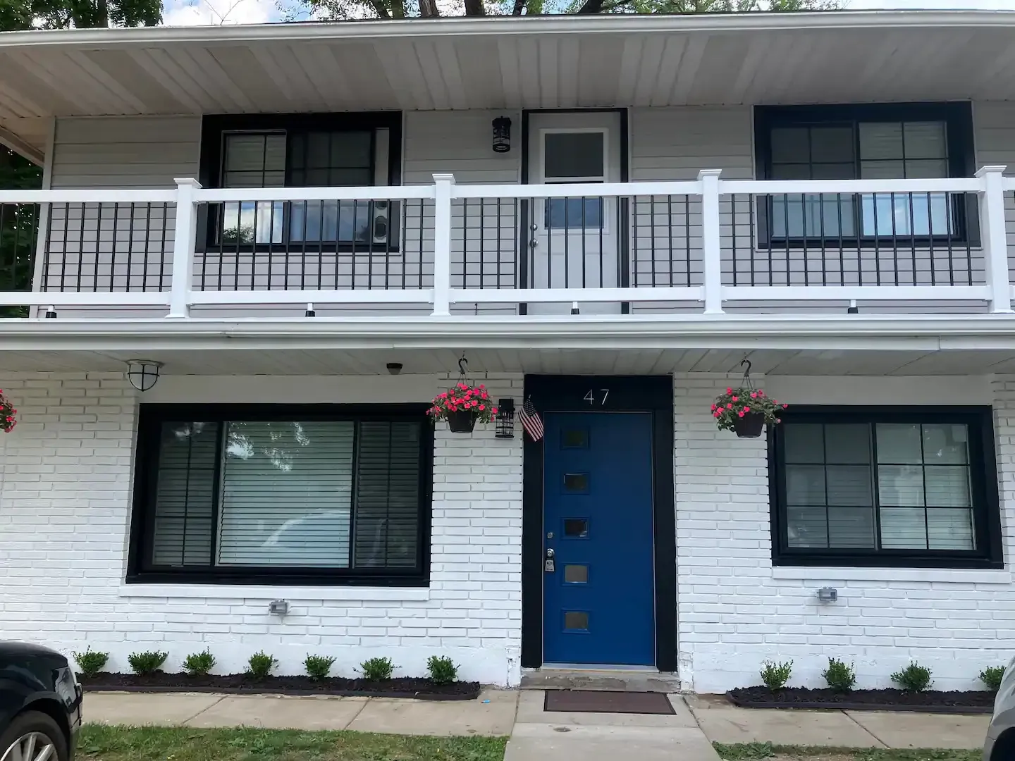 A white brick house with a blue door and a balcony.