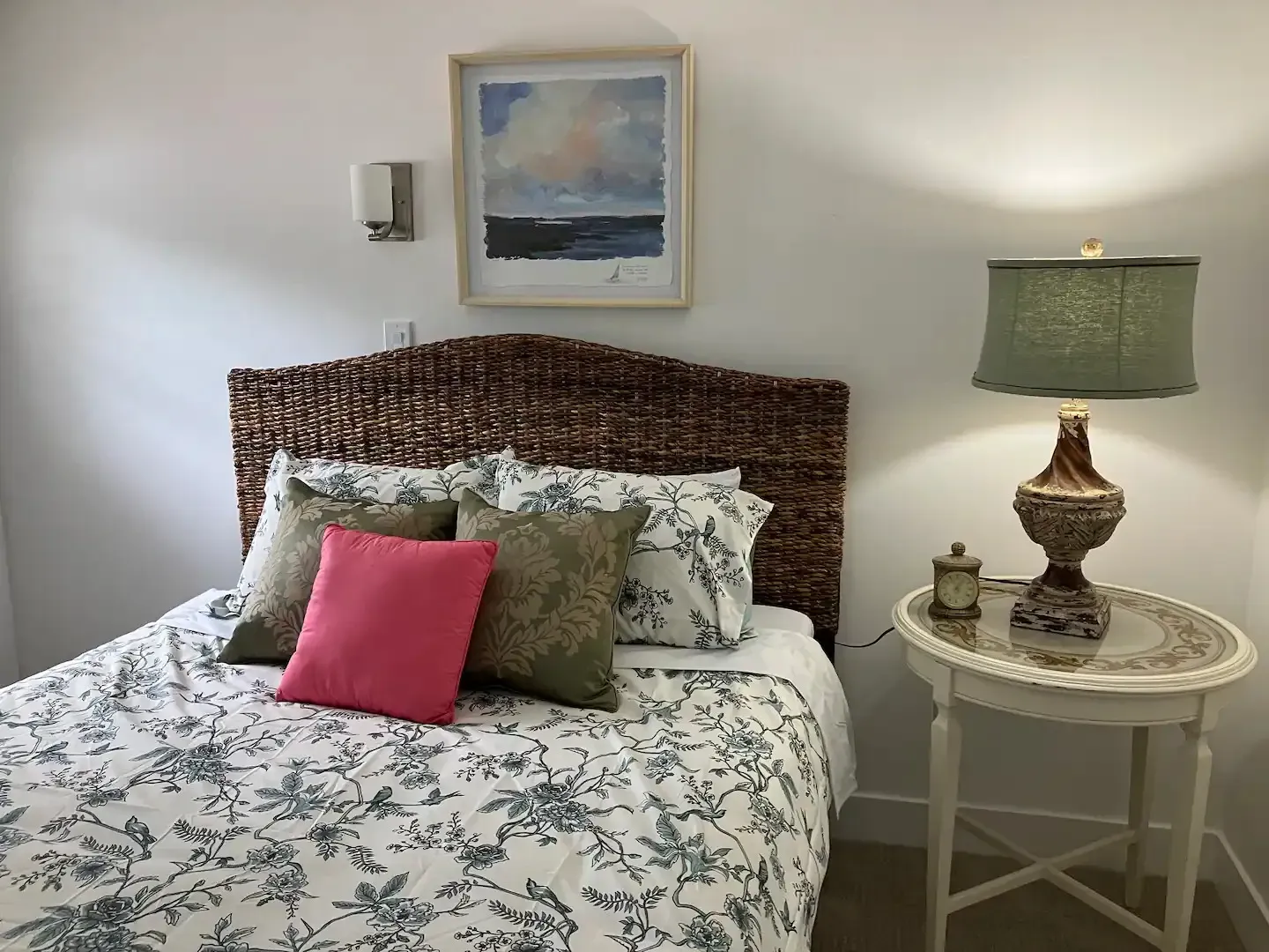 A bedroom with a bed , nightstand , lamp and picture on the wall.