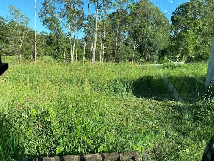 A Tractor is Cutting Grass in a Field With Trees in the Background — Caloundra Landscape Supplies in Caloundra, QLD