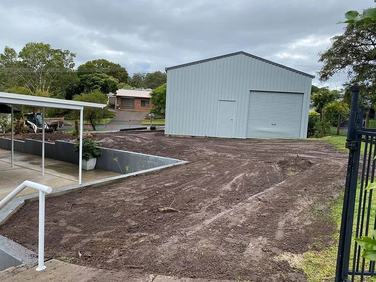 A White Garage is Sitting in the Middle of a Dirt Field Next to a House — Caloundra Landscape Supplies in Caloundra, QLD