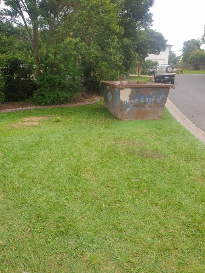 A Dumpster is Sitting on Top of a Lush Green Lawn Next to a Road — Caloundra Landscape Supplies in Caloundra, QLD
