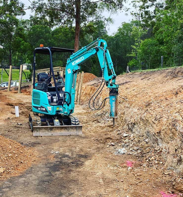 A Blue Kobelco Excavator is Working on a Dirt Road — Caloundra Landscape Supplies in Caloundra, QLD